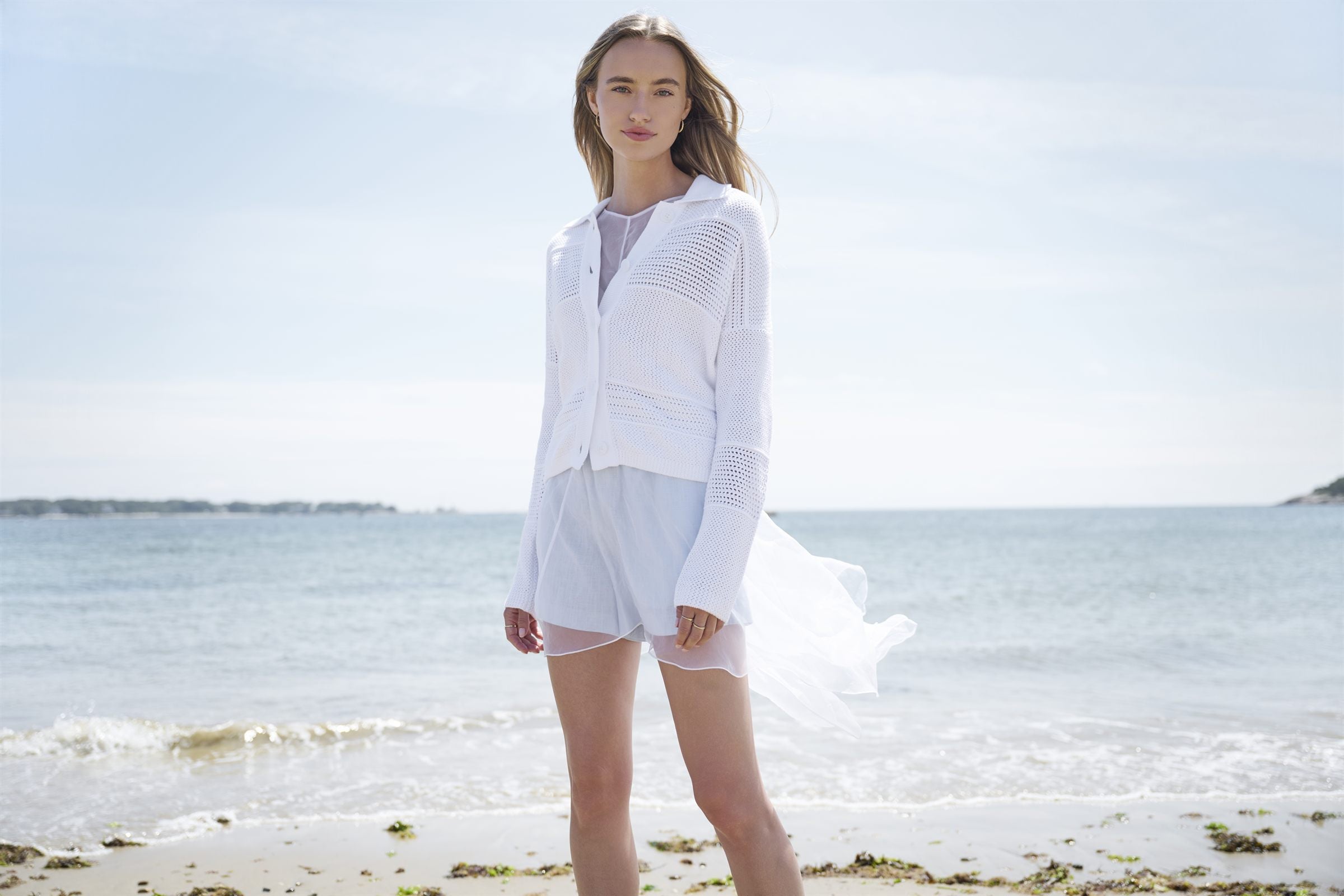 KINROSS model wearing a white knit cardigan by the water